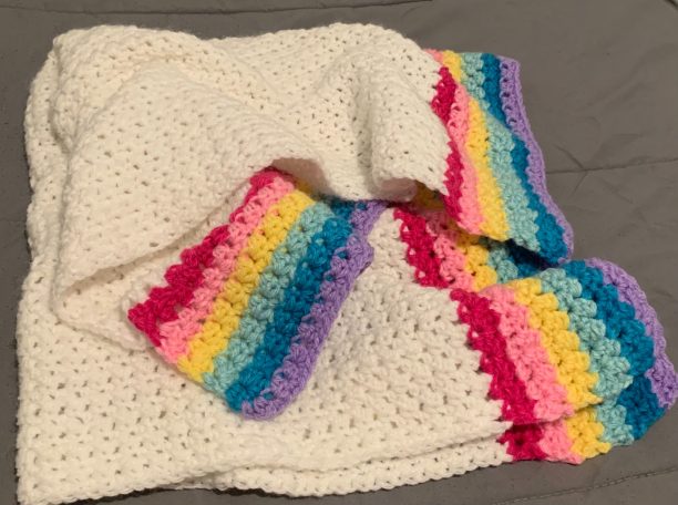 Crocheted whit blanket with red, pink, yellow, teal, blue, and purple border. 