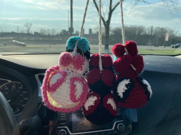 spiderman, miles morales, and spider gwen crochet amigurumi hanging from a crocheted web in a car.